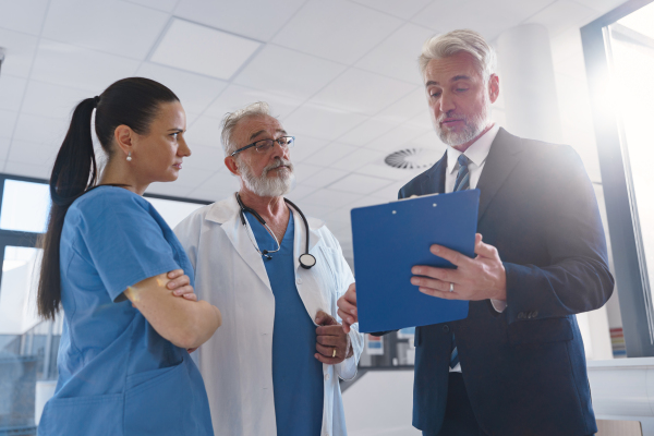 Medical sales representative presenting new medication to doctors, standing hospital hallway. Hospital setting.