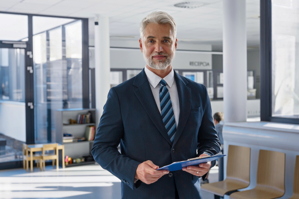 Confident senior manager holding documents in modern clinic or office environment.