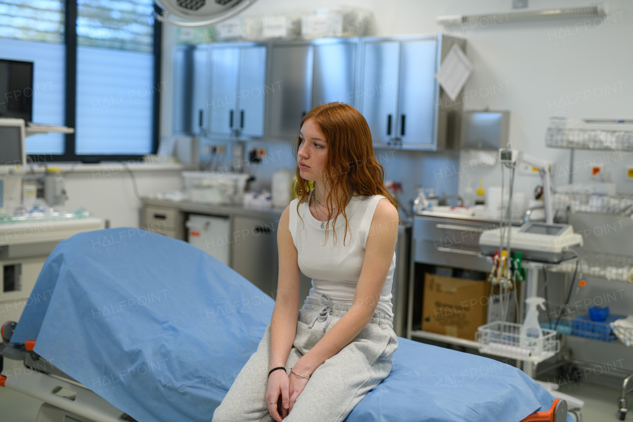 Teenage girl waiting for medical examination in hospital, sitting on examination table.