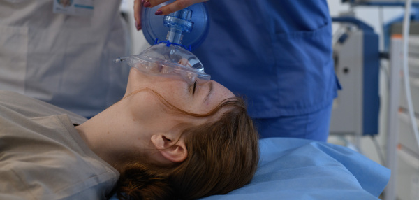 Medical staff applying oxygen mask to unconscious teenage girl in hospital. Medical procedure.