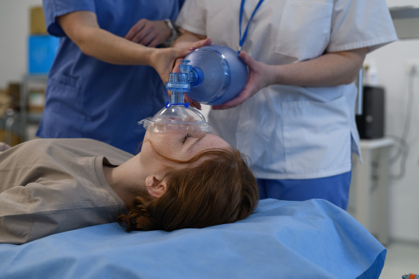 Medical staff applying oxygen mask to unconscious teenage girl in hospital. Medical procedure.