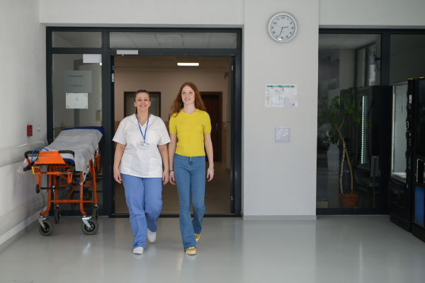 Nurse walking with teenage girl patient in modern hospital waiting room.