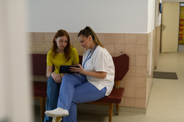 Nurse helping teen girl complete medical intake form in doctors office.