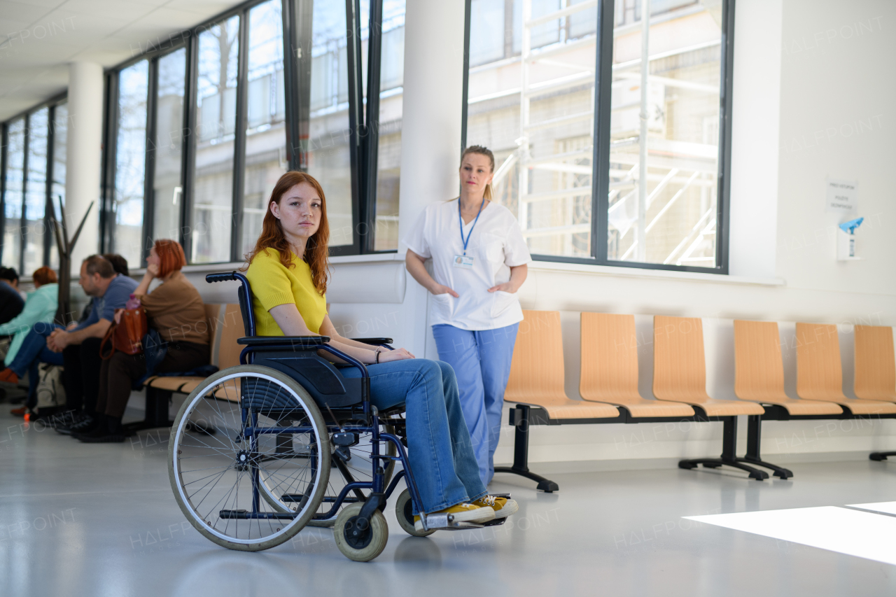 Nurse with young female patient in wheelchair at hospital, modern clinic.