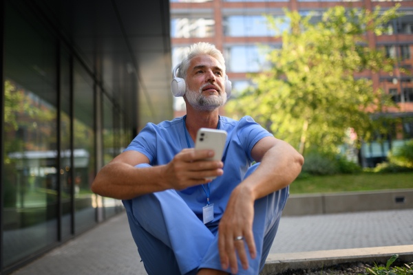 Healthcare worker relaxing with music outside hospital, headphones on head.
