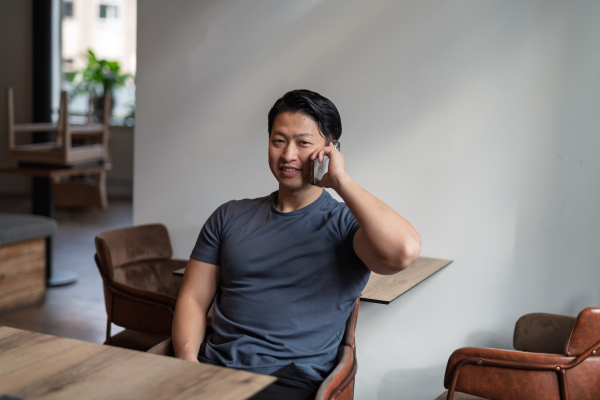 Young asian man talking on smartphone, sitting at empty table.