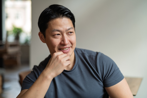 Athletic Asian man looking away in casual setting, smiling.