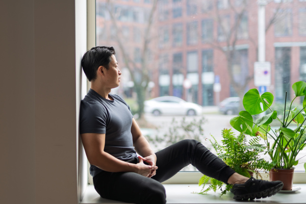 Confident young man sitting by the window in natural light, resting.