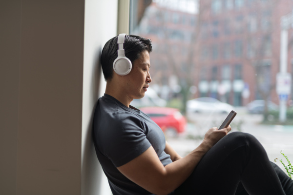 Hygge moment for young man sitting by the window and listening music.