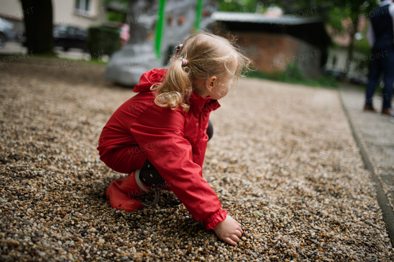 Child in red raincoat spending free time on playground in the city.