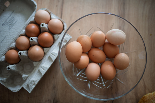 Fresh brown eggs in carton and glass bowl. Farm-fresh eggs on wooden kitchen table.