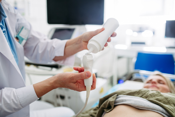 Radiologist applying gel to ultrasound probe before abdominal scan. Medical procedure.