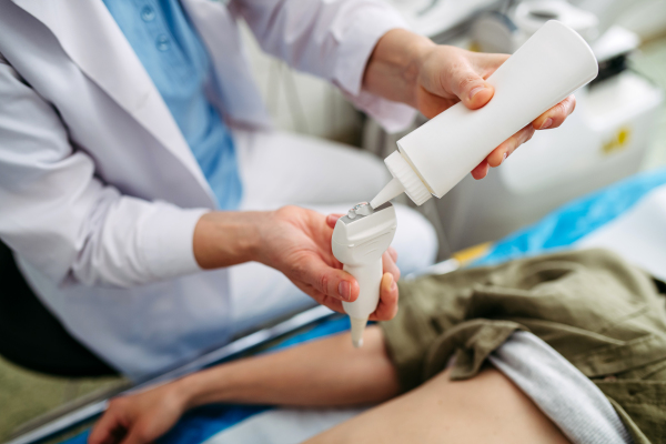 Radiologist applying gel to ultrasound probe before abdominal scan. Medical procedure.