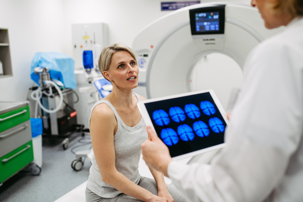 Doctor explaining results from CT scan to patient in diagnostic imaging room. Medical consultation.