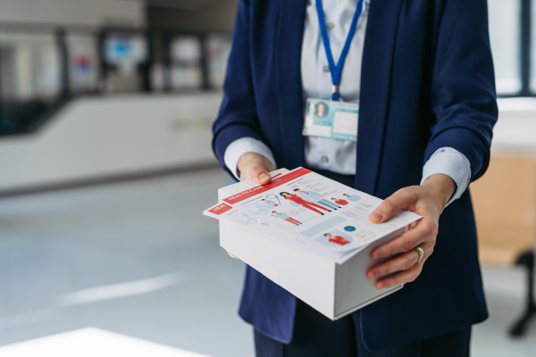 Close up of pharma rep holding box with samples of new medication and flyer, pamphlet.