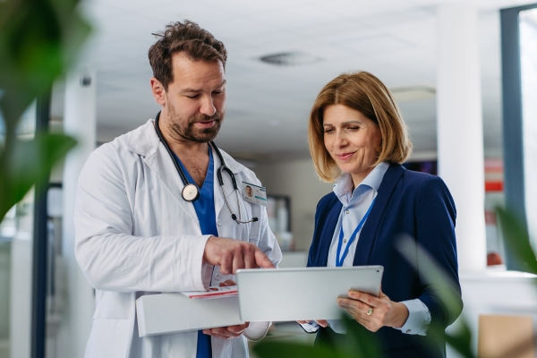 Female medical sales representative presenting medication to doctor, standing in hospital hallway.