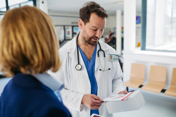 Female medical sales representative presenting medication to doctor, standing in hospital hallway.