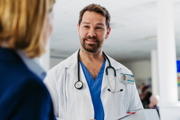 Female medical sales representative presenting medication to doctor, standing in hospital hallway.