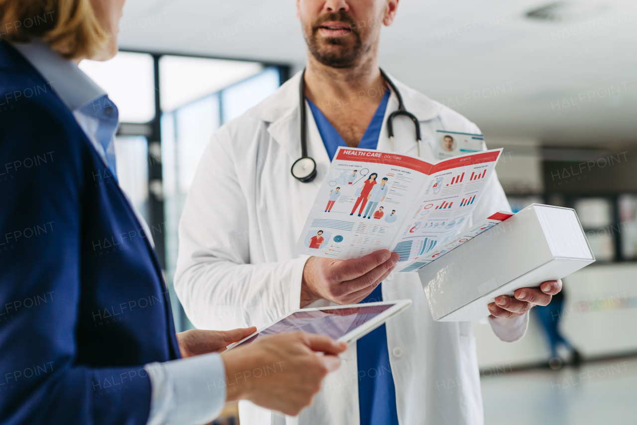 Female medical sales representative introducing pharmaceutical products to doctor. Hospital setting.