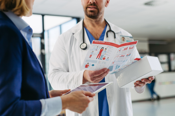Female medical sales representative introducing pharmaceutical products to doctor. Hospital setting.