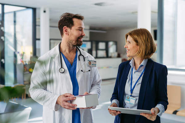 Female medical sales representative presenting medication to doctor, standing in hospital hallway.