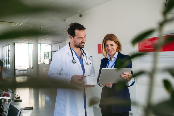 Confident female medical sales representative introducing pharmaceutical products to doctor. Hospital setting.