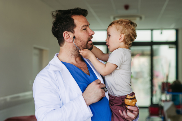 Handsome doctor holding young pediatric patient in arms. Healthcare worker as working father.