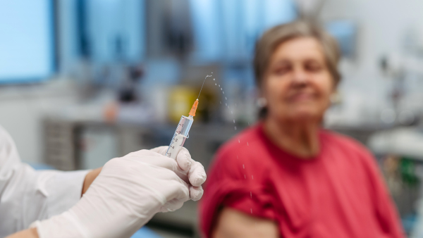Close up of doctor holding injection with vaccine. Elderly patient being vaccinated.