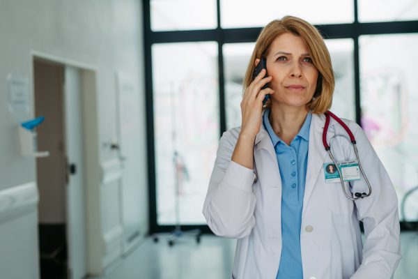 Portrait of female doctor standing in hospital hallway and making phone call.