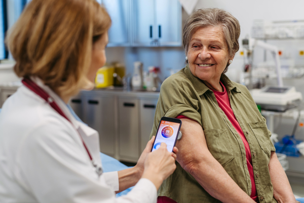 Endocrinologist teaching older patient how to connect continuous glucose monitor with mobil app. Senior health care.