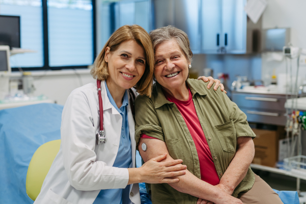Elderly patient and female physician smiling at clinic. Senior health care.