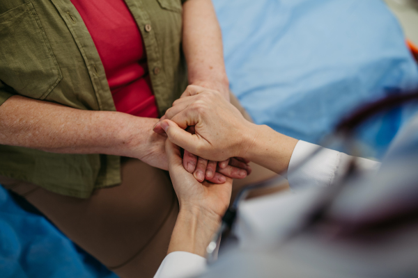 Doctor holding hands with senior patient in compassionate gesture, medical setting.