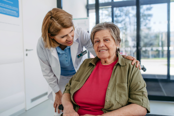 Geriatric doctor talking with patient in a wheelchair in hospital hallway. Senior health care.