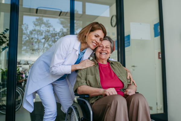 Elderly patient in wheelchair and female physician smiling at clinic. Senior health care.