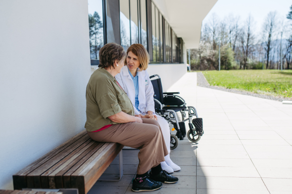 Elderly patient talking with caring female physician in front of hospital. Senior health care.