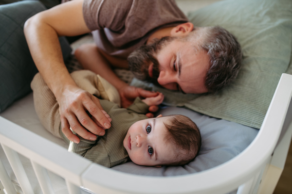 Father putting the baby to sleep, lying next to him in the crib and soothing him.