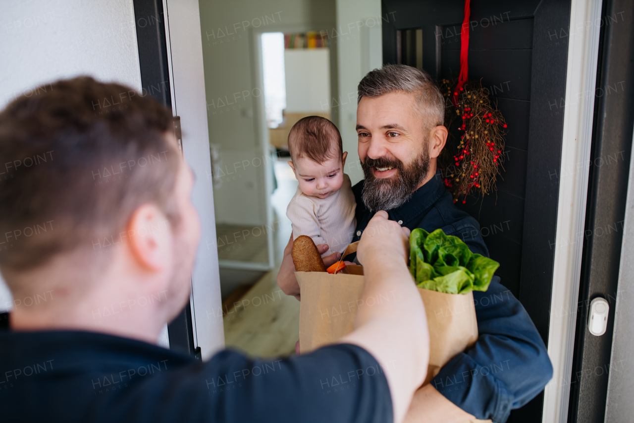 Father holding a baby in his arms receiving a grocery delivery. Online grocery delivery service.