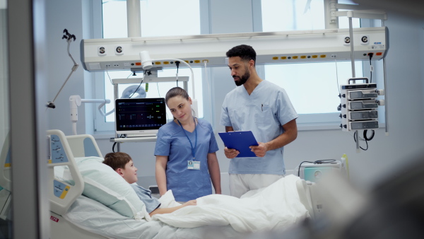 A nurse and doctor caring for young boy patient lying in hospital bed.