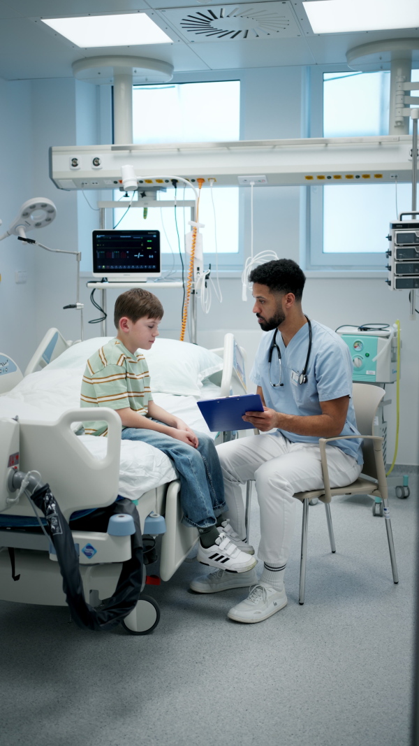 Male doctor examining young boy patient sitting on hospital bed.