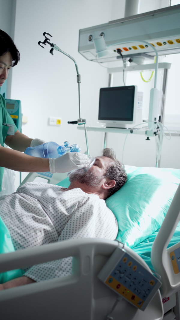 Male doctor providing oxygen ventilation to unconscious patient in hospital.