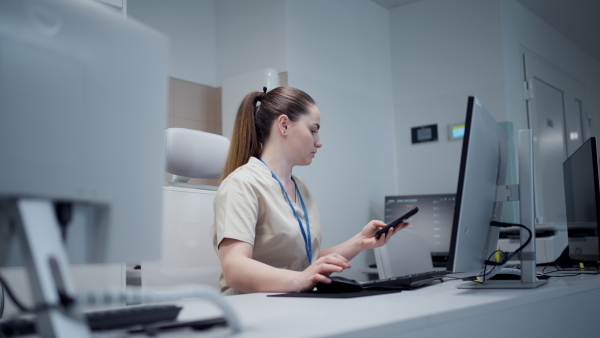 Smiling young nurse in hospital, working on computer and having a call.