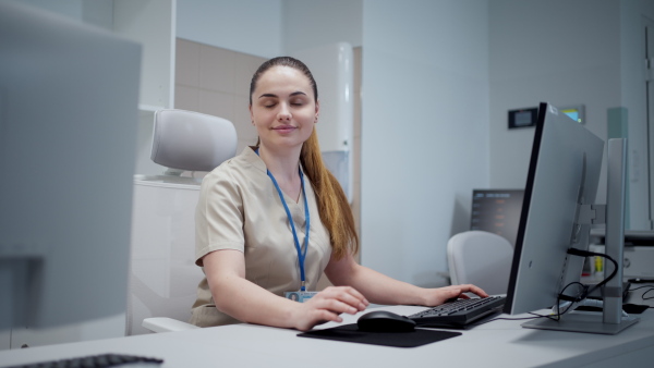 Smiling young nurse in hospital, working on computer.