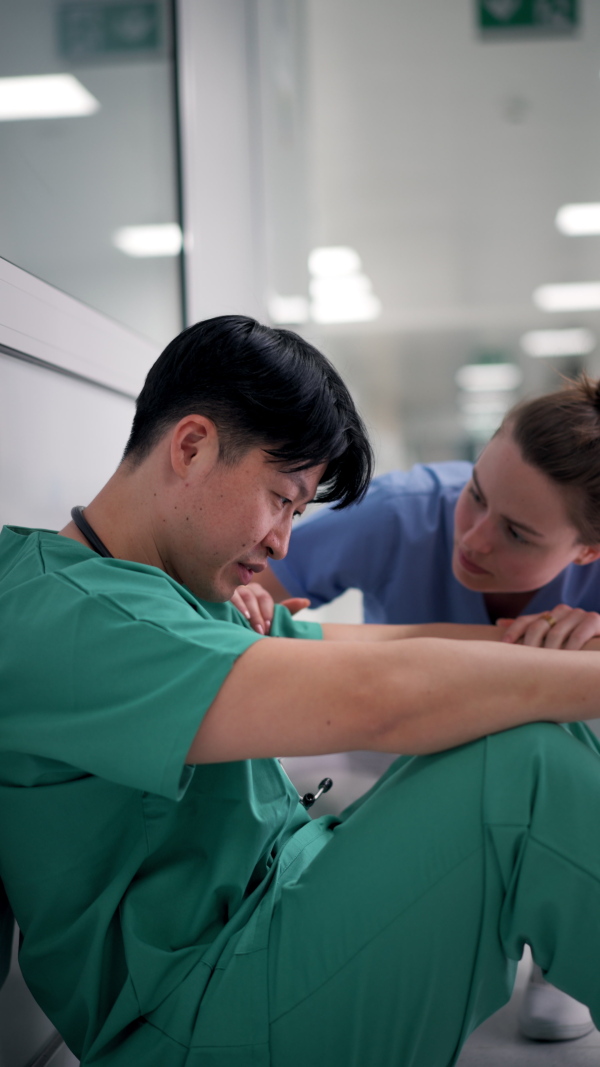 Nurse comforting a doctor after unsuccessful surgery in hospital corridor.