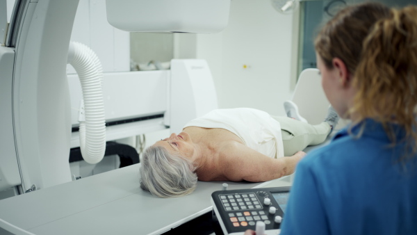 Nurse positioning elderly patient on tilting fluoroscopy table for X-ray scan