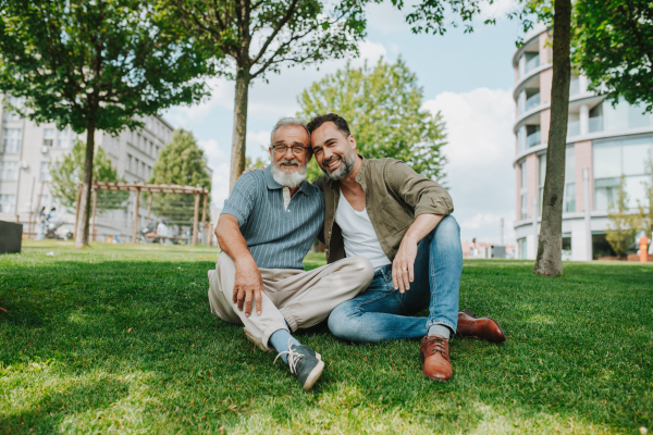 Father and adult son sitting on grass in park, sharing a story from the past. Fathers day concept.
