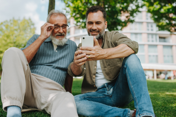 Son showing older father something in smartphone, sharing a joyful moment outdoors