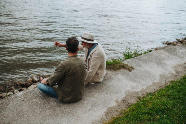 Father and adult son sharing a peaceful moment, lookign at river. Fathers day concept.
