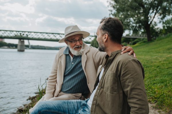 Father and adult son sharing a peaceful moment, lookign at river. Fathers day concept.