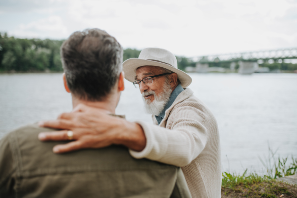 Father and adult son sharing a peaceful moment, lookign at river. Fathers day concept.