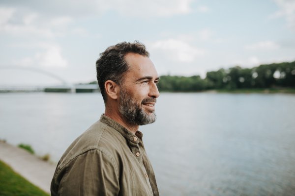Confident middle-aged man standing on river bank, looking at water.